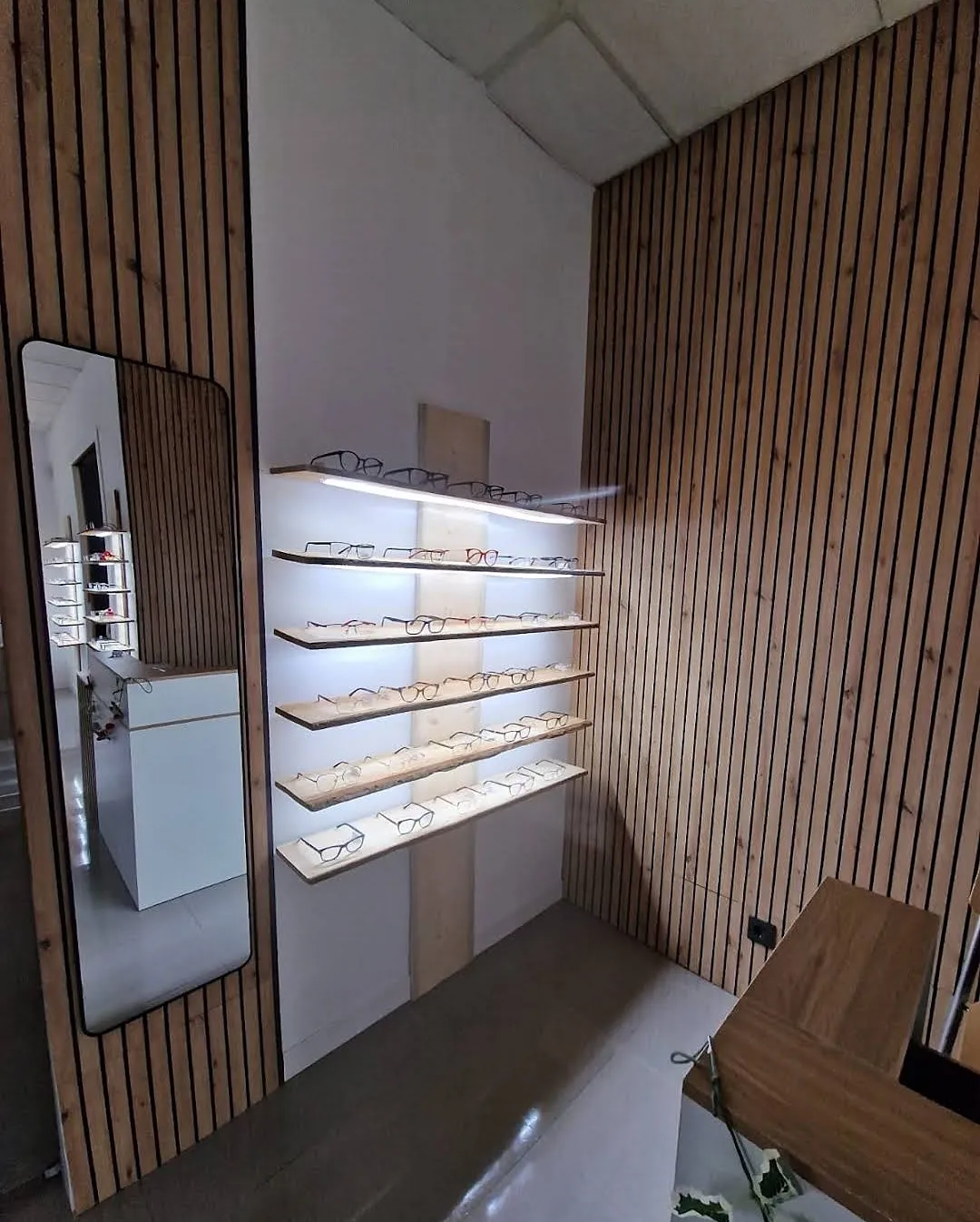 Expositor de gafas iluminado junto a la pared de listones de madera